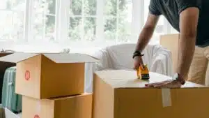 Uomo che sigilla uno scatolone da trasloco in un appartamento con nastro adesivo
